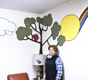 Volunteer and “artist in residence” Jo Beth Lehrer by part of the mural she created for HOPE’s youth counseling room.