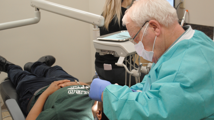 Dentist David Dasher, director of Amaus Dental Clinic in downtown Syracuse, treats a patient. The clinic offered free dental services to about 700 patients in 2018. In the back is volunteer dental assistant Rebecca Vignogna.